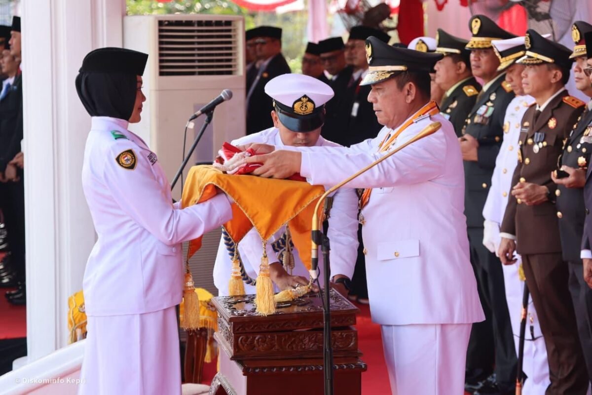 Gubernur Kepulauan Riau Ansar Ahmad menyerahkan Bendera Merah Putih kepada Yuanita Putri Verinda, pembawa baki Paskibraka dalam Upacara Peringatan HUT ke-81 Republik Indonesia di Gedung Daerah Tanjungpinang, Senin (17/8/2026). Foto: Diskominfo Kepri